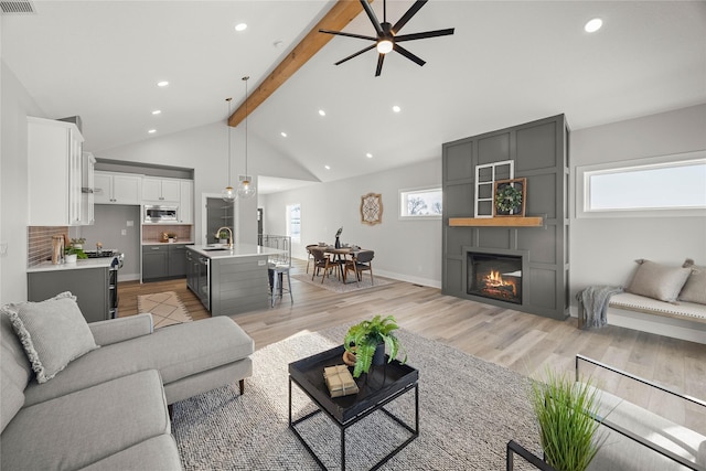 living room with sink, ceiling fan, vaulted ceiling with beams, light hardwood / wood-style floors, and a large fireplace