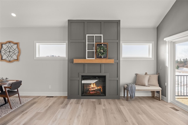 living area with a large fireplace, a healthy amount of sunlight, and light hardwood / wood-style flooring