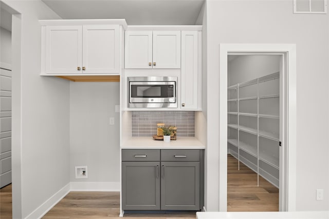 kitchen featuring gray cabinetry, stainless steel microwave, white cabinets, and tasteful backsplash