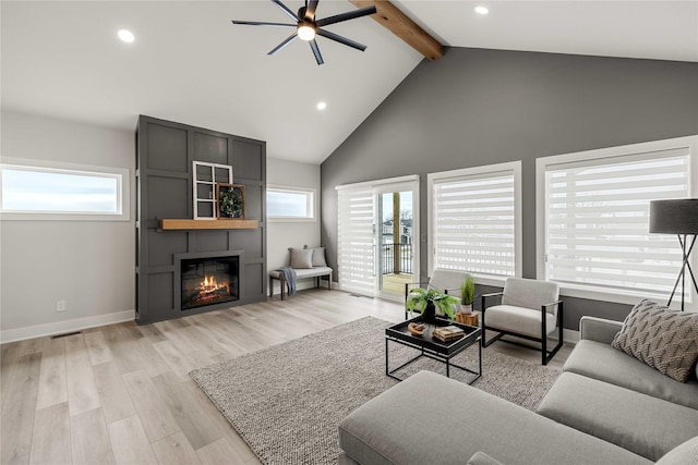 living room with a fireplace, beamed ceiling, plenty of natural light, and light hardwood / wood-style flooring