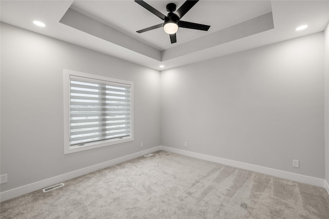 carpeted spare room featuring ceiling fan and a raised ceiling