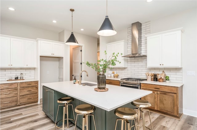 kitchen with white cabinets, sink, wall chimney range hood, and an island with sink