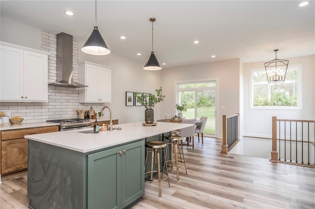 kitchen with stainless steel gas range oven, wall chimney range hood, decorative light fixtures, a center island with sink, and white cabinetry