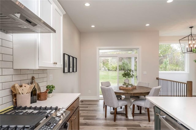 kitchen featuring backsplash, an inviting chandelier, wall chimney exhaust hood, decorative light fixtures, and white cabinetry