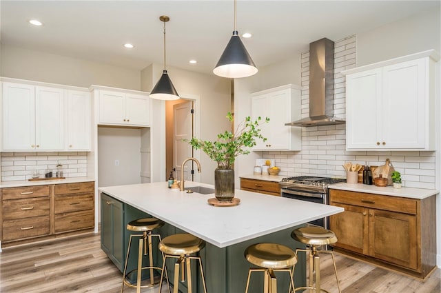 kitchen with white cabinets, wall chimney range hood, and a kitchen island with sink