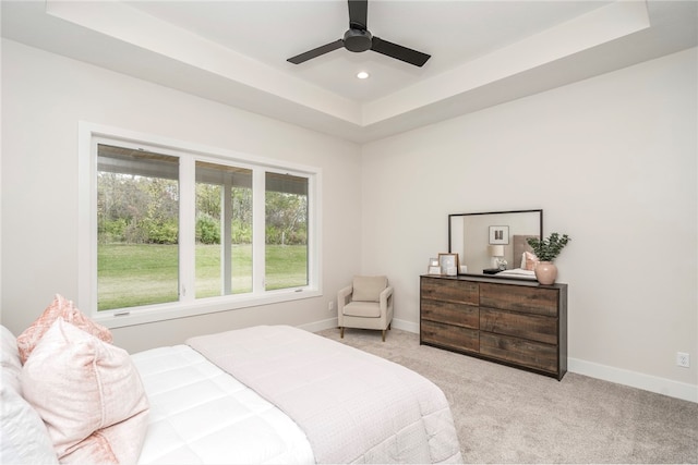 carpeted bedroom with a raised ceiling and ceiling fan