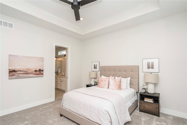 bedroom with ceiling fan, light colored carpet, connected bathroom, and a tray ceiling