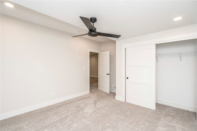 unfurnished bedroom featuring light carpet, a textured ceiling, a closet, and ceiling fan