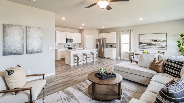 living room featuring ceiling fan, sink, and light wood-type flooring