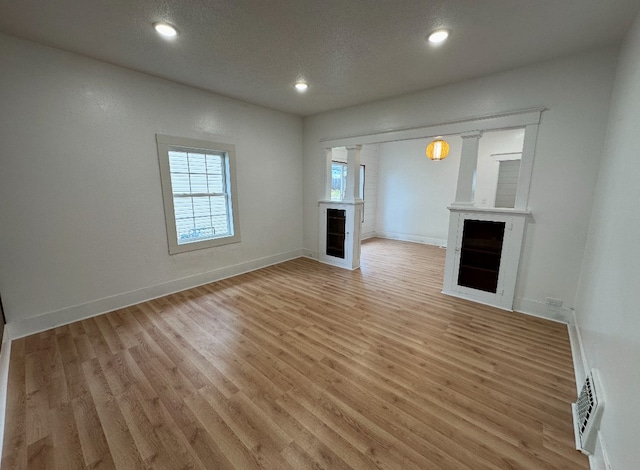 unfurnished living room featuring light hardwood / wood-style floors, a textured ceiling, and a large fireplace