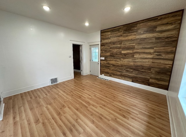 unfurnished room featuring wood walls, a textured ceiling, and light hardwood / wood-style flooring