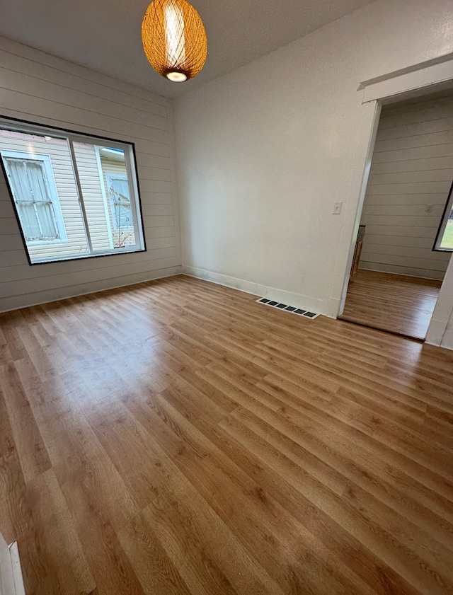 spare room featuring wood walls and light hardwood / wood-style flooring