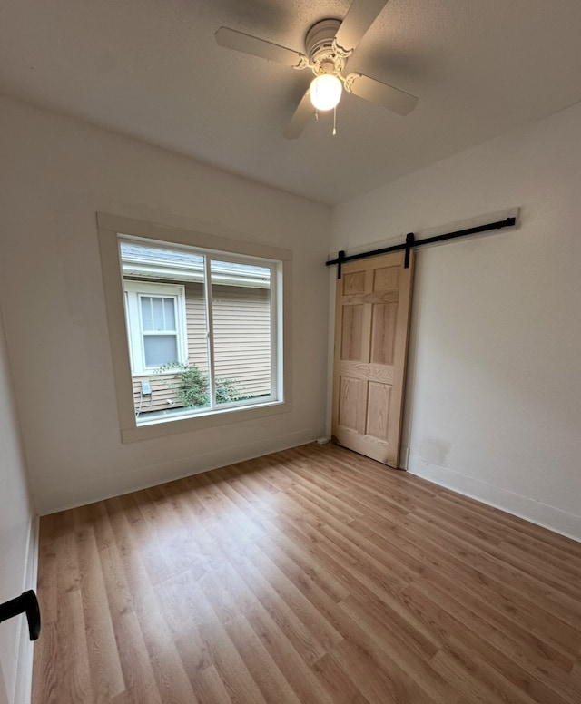 unfurnished bedroom with a barn door, light hardwood / wood-style floors, and ceiling fan