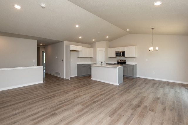 kitchen with light wood-type flooring, appliances with stainless steel finishes, gray cabinets, an island with sink, and lofted ceiling