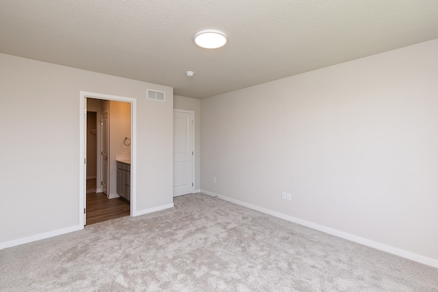 unfurnished bedroom with a textured ceiling, carpet floors, and ensuite bath