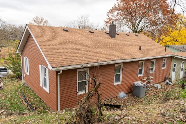 back of house featuring roof with shingles and a chimney