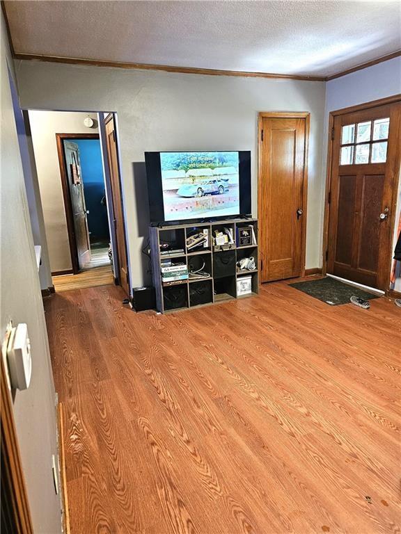 living area with ornamental molding, wood finished floors, baseboards, and a textured ceiling