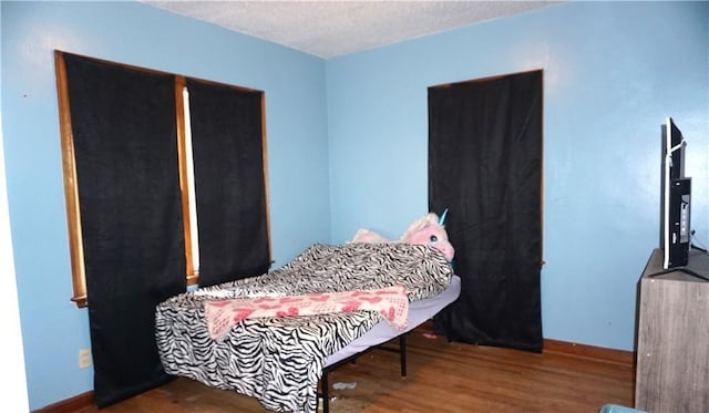 bedroom with a textured ceiling, baseboards, and wood finished floors