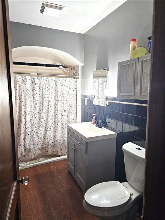 bathroom with visible vents, toilet, vanity, wood finished floors, and tile walls