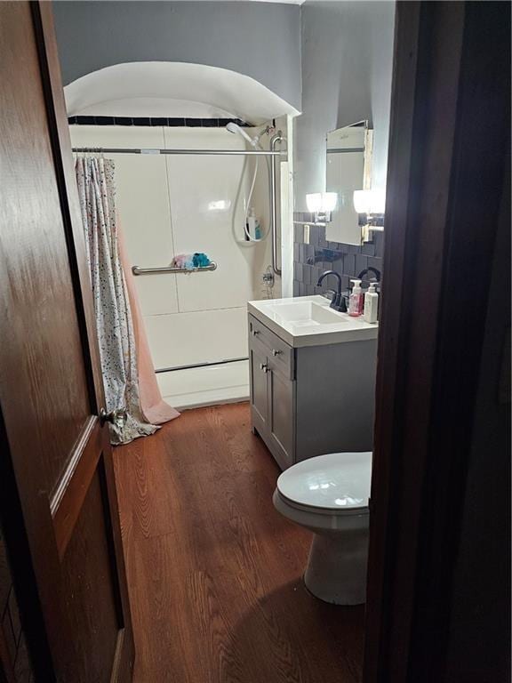 full bathroom with toilet, a shower with curtain, wood finished floors, decorative backsplash, and vanity