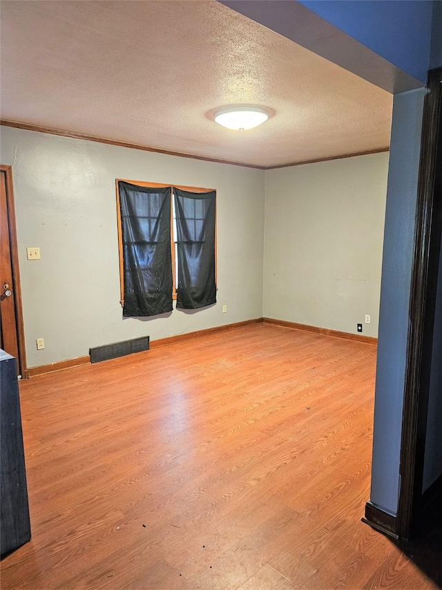 spare room with baseboards, wood finished floors, visible vents, and a textured ceiling