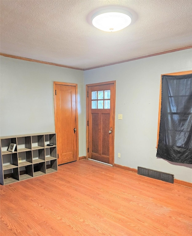 entryway with ornamental molding, wood finished floors, visible vents, and a textured ceiling