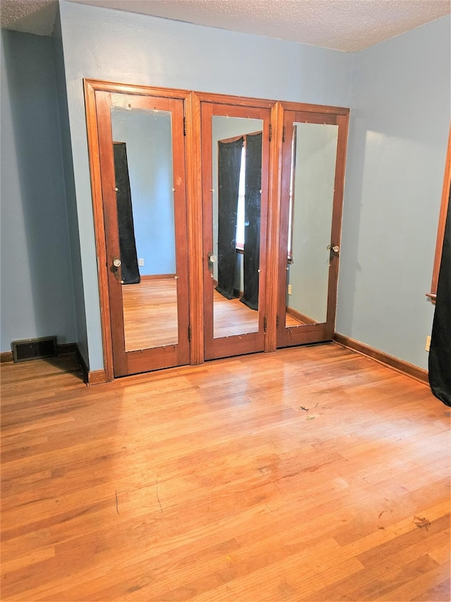 empty room featuring visible vents, baseboards, a textured ceiling, and light wood finished floors