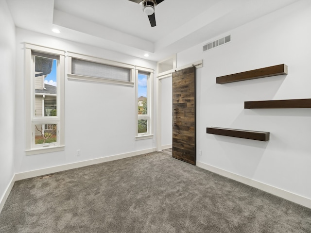 carpeted spare room with a barn door, ceiling fan, and a healthy amount of sunlight