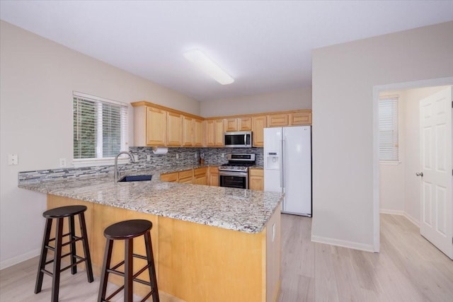 kitchen with light stone countertops, sink, stainless steel appliances, kitchen peninsula, and light wood-type flooring