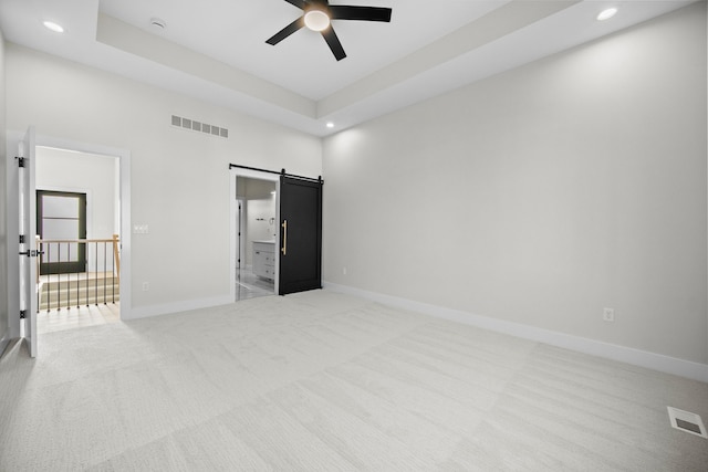 bedroom with a barn door, light colored carpet, visible vents, baseboards, and a raised ceiling