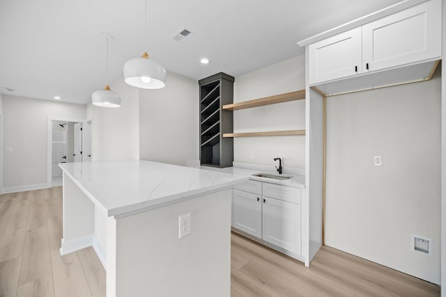 kitchen with light stone counters, a sink, visible vents, light wood-type flooring, and a center island