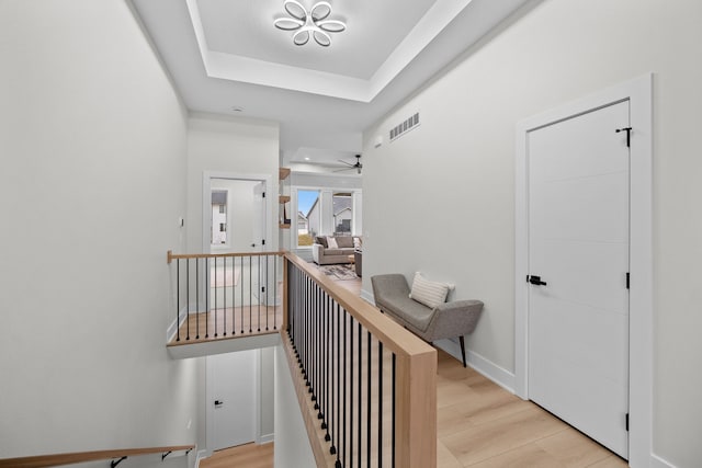 corridor featuring light wood-style flooring, a raised ceiling, visible vents, and baseboards