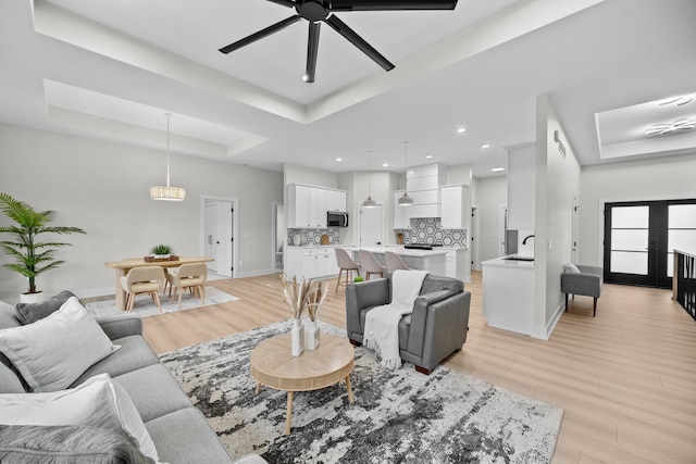 living area featuring ceiling fan, recessed lighting, baseboards, light wood-style floors, and a raised ceiling