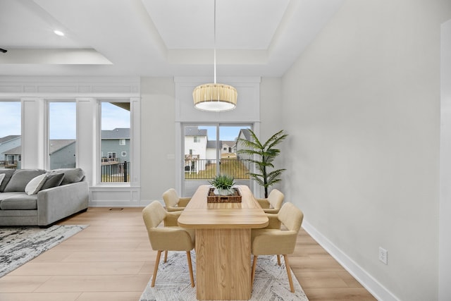 dining room featuring a tray ceiling, light wood-style flooring, and baseboards