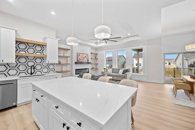 kitchen with tasteful backsplash, dishwasher, a glass covered fireplace, a tray ceiling, and light wood-type flooring