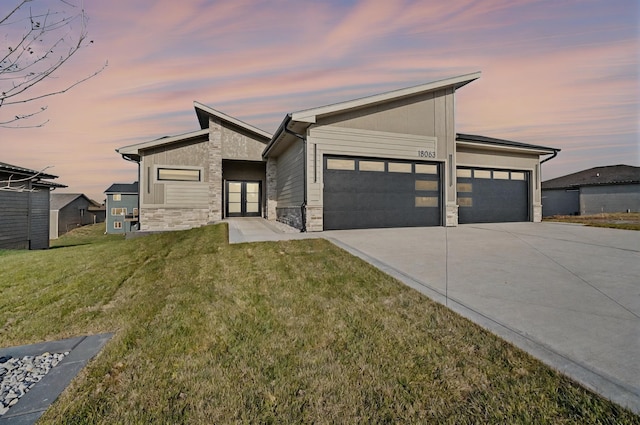 modern home featuring a garage, stone siding, a yard, and concrete driveway