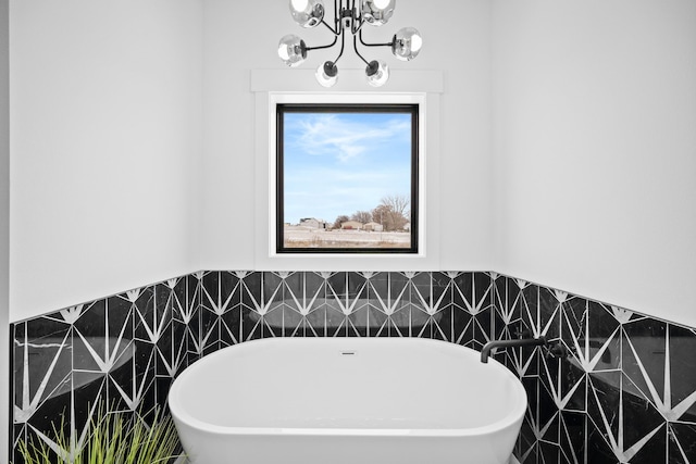 bathroom with an inviting chandelier, tile walls, and a tub