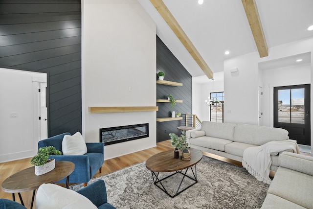 living room featuring wood walls, an inviting chandelier, beamed ceiling, a large fireplace, and wood-type flooring