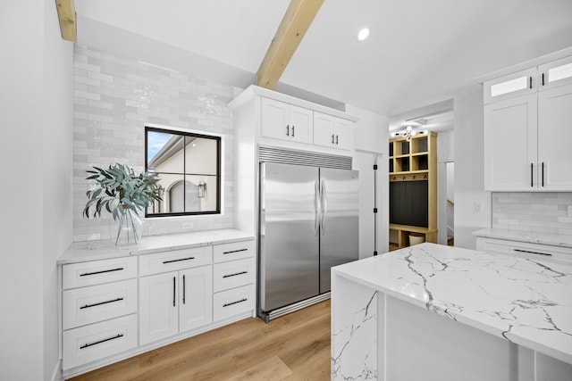 kitchen with backsplash, built in refrigerator, light stone countertops, light wood-type flooring, and white cabinetry