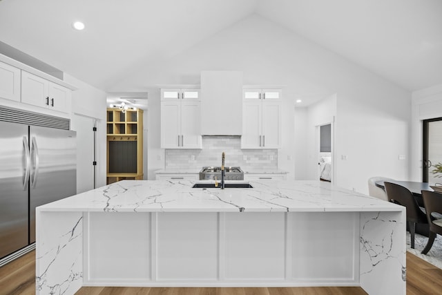 kitchen with white cabinetry, stainless steel built in fridge, a kitchen island with sink, and custom exhaust hood