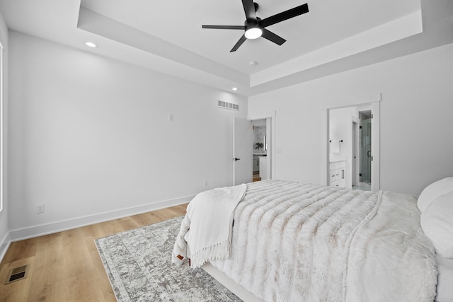 bedroom with ceiling fan, light hardwood / wood-style floors, and a tray ceiling