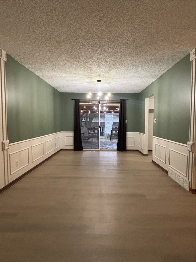 unfurnished dining area featuring an inviting chandelier, hardwood / wood-style floors, and a textured ceiling