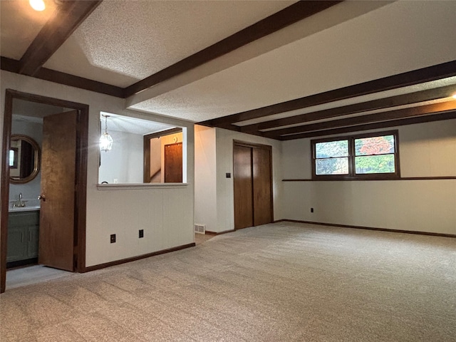 empty room with a textured ceiling, elevator, light colored carpet, and beam ceiling