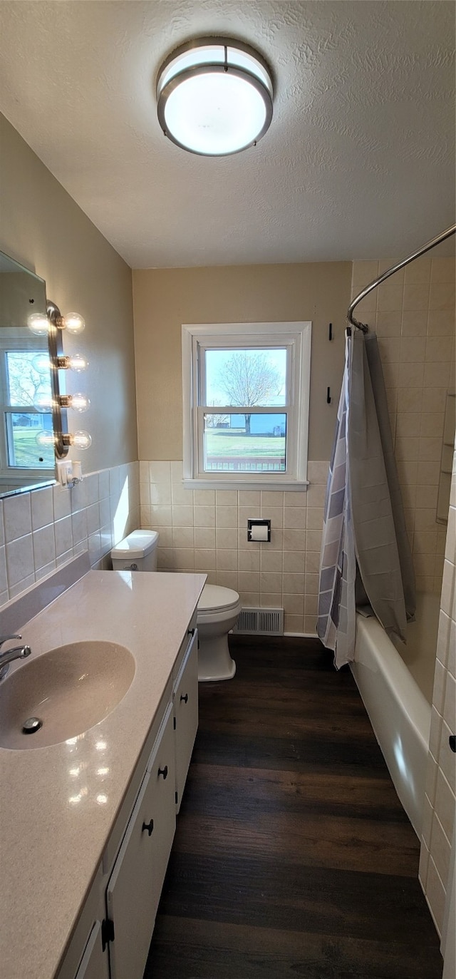 full bathroom with tile walls, wood-type flooring, vanity, a textured ceiling, and shower / bath combo with shower curtain