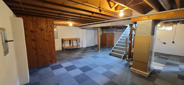 basement with wood walls, electric panel, and heating unit