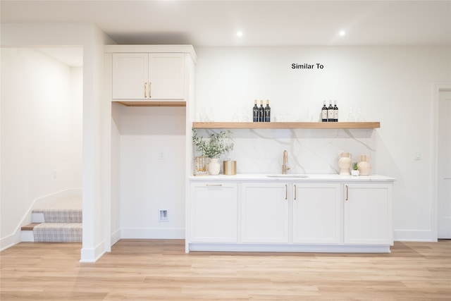 bar featuring decorative backsplash, sink, light hardwood / wood-style floors, and white cabinets