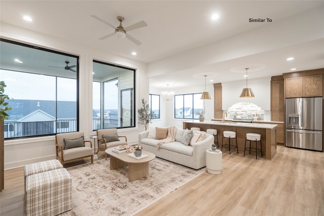 living room with ceiling fan with notable chandelier, light hardwood / wood-style flooring, and sink