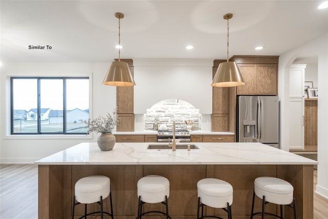 kitchen featuring stainless steel fridge, light wood-type flooring, light stone countertops, hanging light fixtures, and sink