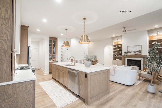 kitchen featuring stainless steel appliances, hanging light fixtures, sink, an island with sink, and light hardwood / wood-style flooring