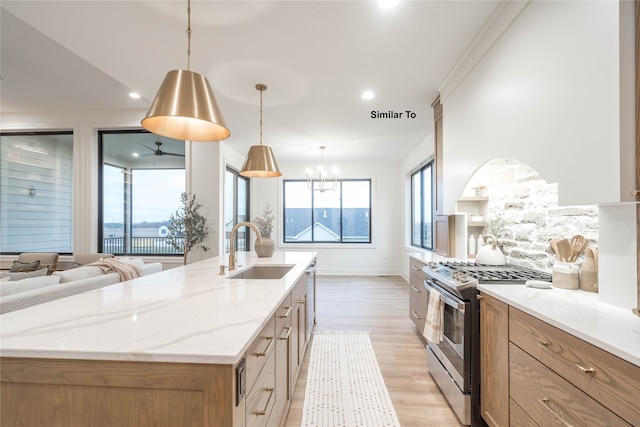 kitchen featuring light wood-type flooring, decorative light fixtures, a large island with sink, stainless steel gas range oven, and sink